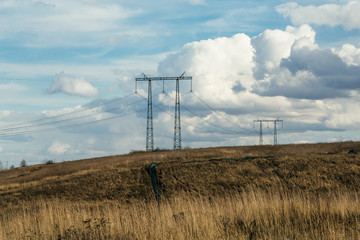 Power lines in the field. Power lines in a spring field against a blue sky and white clouds. Electricity and electrification concept