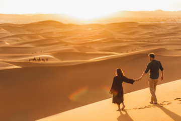 Couple walking in Sahara desert at sunset. View from behind, nature background. Travel, freedom and wanderlust concept.