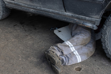 Mechanic in  uniform lying down and working under car at the garage.