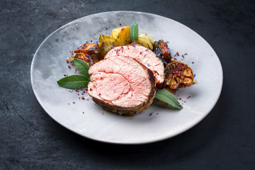 Traditioneller gegrillter Kalbsrollbraten angeboten mit Bratkartoffel, Karotten und Zwiebel als closeup auf einem Modern Design Teller mit Textfreiraum