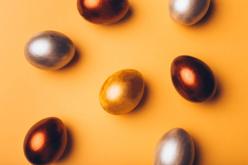 Bronze, silver and gold easter eggs on a yellow background.
