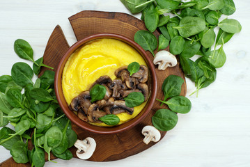 Corn porridge (polenta) with mushrooms in a brown plate on the white surface. Healthy homemade food