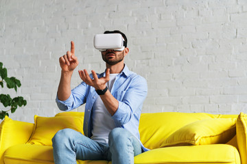 Front view of man using virtual reality glasses, showing one hand up and holding something in another hand