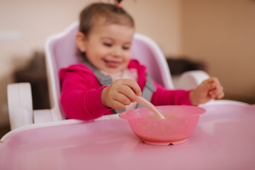 Little cute baby girl are eating in hight chair. Portrait of little smiled child at home