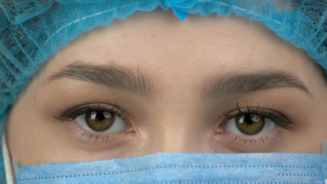 Close-up of a young woman doctor eyes. Wearing blue protective mask and cap.