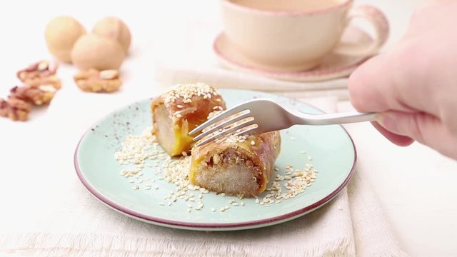 Baklava, traditional arabic sweets is cut with a fork in blue ceramic plate on a whte background. side view, close up.
