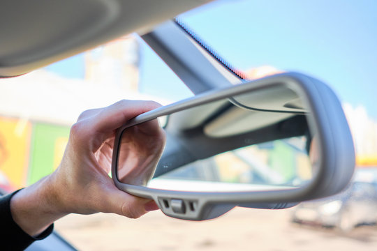 A man in a modern car. Hand adjusts the rearview mirror.