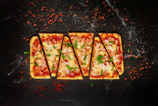 Sliced Hawaiian pizza on black stone background, top view.