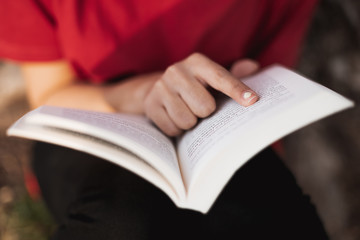 Close up of a open book right in the middle by a young female who is pointing her finger in a word of the page. Low depth of field.
