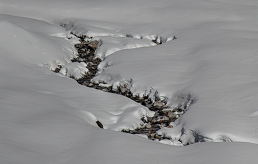 Mountain creek snaking through heavy snowfield