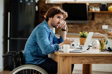 Young freelancer in wheelchair text messaging on smart phone while working at home.