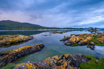 Night sea shore landscape with small rocks and highlands of Skye island at the horizon. Hebrides archipelago, Scotland.