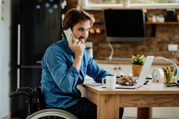 Happy disabled businessman talking on the phone while working on laptop at home.