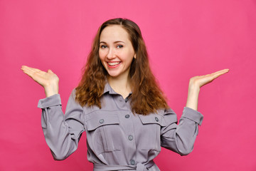 Stylish caucasian girl in a gray dress and holds abstract objects on the palms of her hands on a pink background. Copy space.
