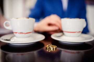 Two cups of coffee on the table with blurred background. Wedding ring between two cups.