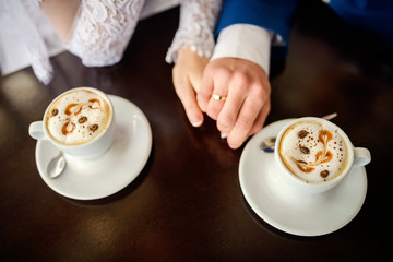 Women's and men's hands with wedding rings, at the cafe table with two cups of coffee on front view.