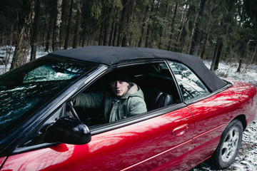 young driver in a red convertible car in a winter forest.