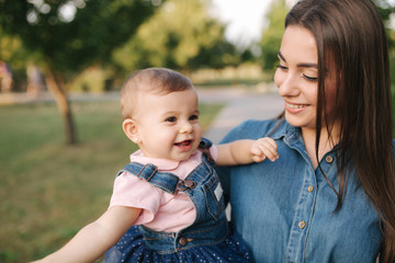 Cute baby on mom's hands outside. Family in the park in summer. Denim style. Mom and daughter in jeans