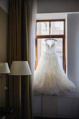 Elegant wedding white dress hanging on a wooden window during a wedding preparation. Bride's morning. Before ceremony