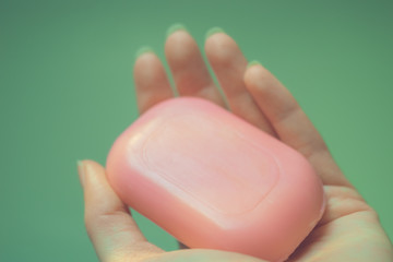 Female fingers hold orange bar of soap closeup. Green background.