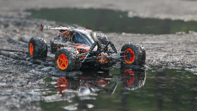 Dirty, orange RC-Car got stuck in the mud on a wet forest mire path. 4KHD