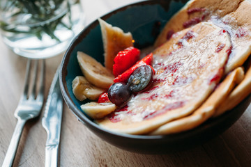 Portion of pancakes with fruits on wooden table with fork knife and water