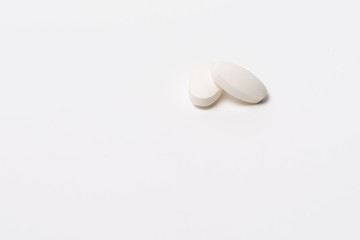 Two white tablet oval shaped on a white background. One lies on the other on top