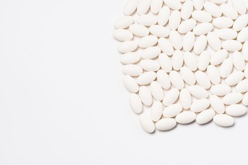 A large number of tablets of white oval-shaped tablets on a white background. View from above