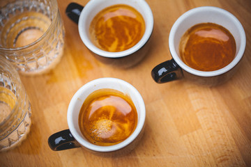 Three aromatic espresso coffee cup and glasses with water on wooden table