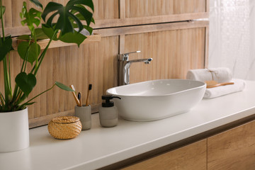 Toiletries and stylish vessel sink near wooden wall in modern bathroom