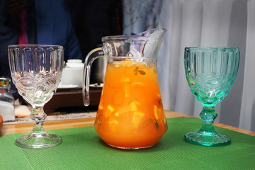 Jug with orange juice and two glasses - white and green on a table in a restaurant
