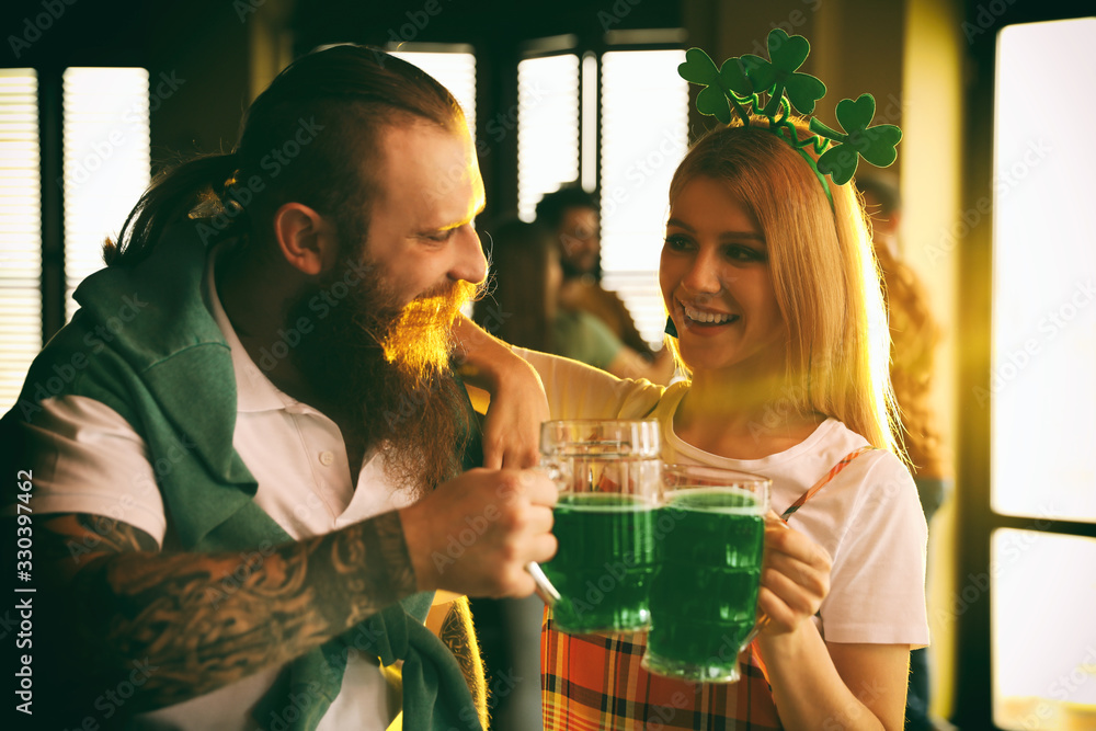 Wall mural Young woman and man toasting with green beer in pub. St. Patrick's Day celebration