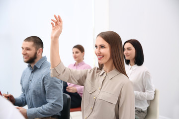 Young woman raising hand to ask question at business training indoors