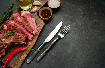 Grilled beef steak with spices and cutlery on a cutting board on a stone background with copy space for your text