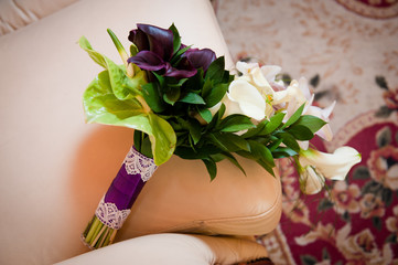 Delicate bouquet of purple and white flowers lying on the sofa. Unusual wedding stylish bouquet with pink and white flowers, wedding dress, details