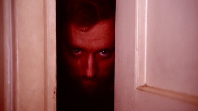 Horror crazy killer waiting for victim in darkness behind the doors. Dangerous thief with monster's eyes intending to attack victim, planning of robbery and violence, criminal aggression concept