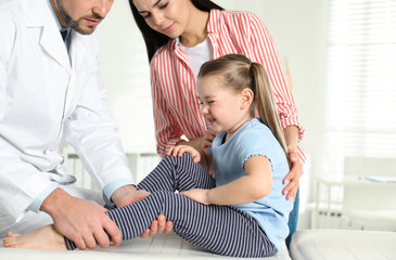 Professional orthopedist examining little patient's leg in clinic