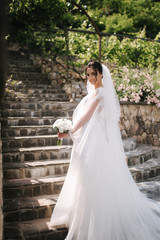Back view of Gorgeous bride stand on the stairs in elegant wedding dress with bouquet of white flowers in her wedding day