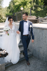 Fototapeta premium Beautiful bride with her handsome groom walking outside on theri wedding day. Happy newlyweds