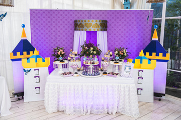 Little girl birthday party table with princess cake, macaroons, cupcakes, and sugar cookies. Candy bar for kids. Sweet holiday buffet with sweets and other desserts.