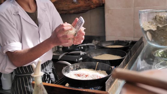 Close-up. Chief grating a cheese, cooking classical Jewish Yemenite food. Cosy and bright street restaurant. Sunlight.