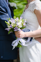 Beautiful wedding bouquet in bride's hands, wedding dress, details. The girl in a white dress holding a bouquet of white, pink flowers and greenery, decorated with silk ribbon