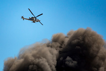 Helicopter flies over large smoke cloud from exploded munitions