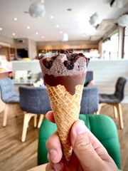 Chocolate ice cream cone on interior cafe background. Hand holding ice cream in waffle cup.