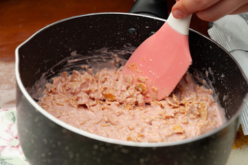Woman's hand making corn flakes in melted strawberry chocolate in the pan. Close-up. Horizontal shot.