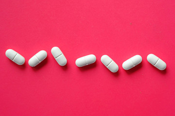 close up of white pills spilling on a red background 