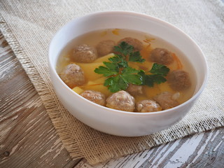 Soup with meatballs and potatoes on a white wooden table