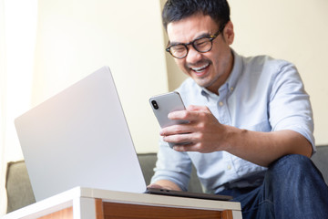 using computer,cell phone.asian man hand typing message keyboard laptop chatting.search information form internet while sitting on sofa.concept for use technology device contact communication business