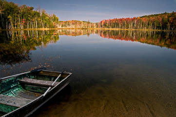 Sunrise light on fall colors at Red Jack Lake in Hiawatha National Forest with fishing boat in foreground.