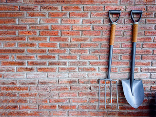 Shovel and rake on red brick wall. Gardening tools background